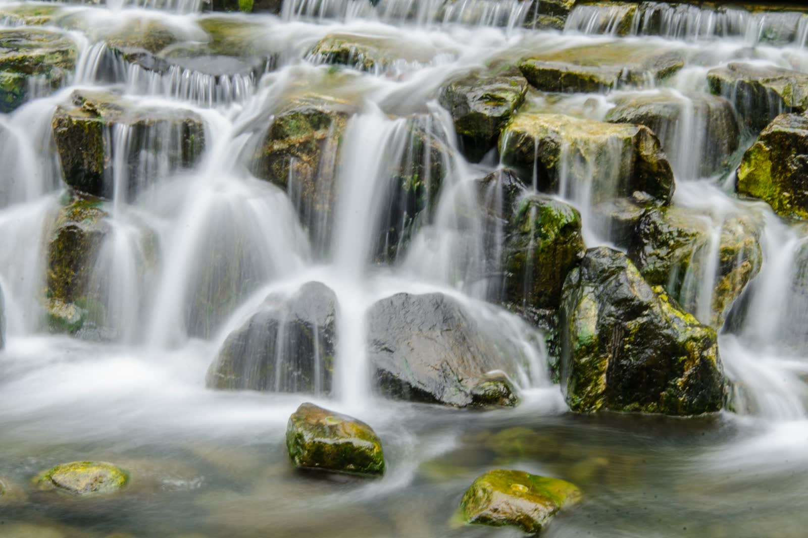 Long-exposure shot of a small stream flowing over moss-covered rocks, water rendered soft and silky against green moss.