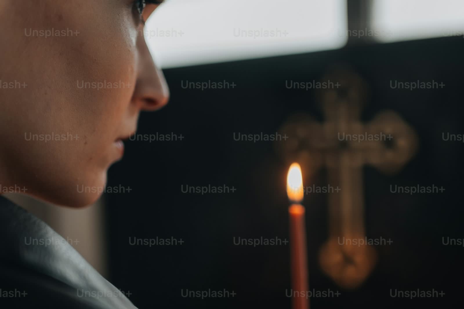 A close-up of a person's hand holding a single lit candle against a dark background, evoking quiet contemplation.