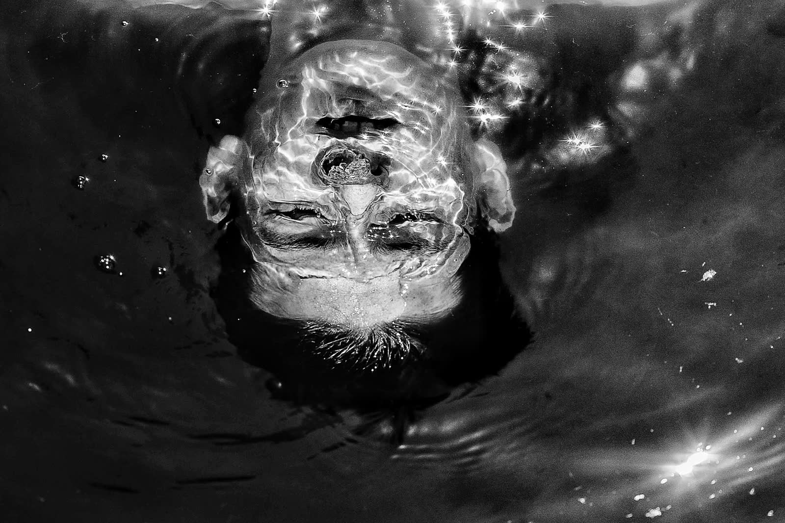 Grayscale photo of a man's facial features reflected in the mirror-like surface of still water.