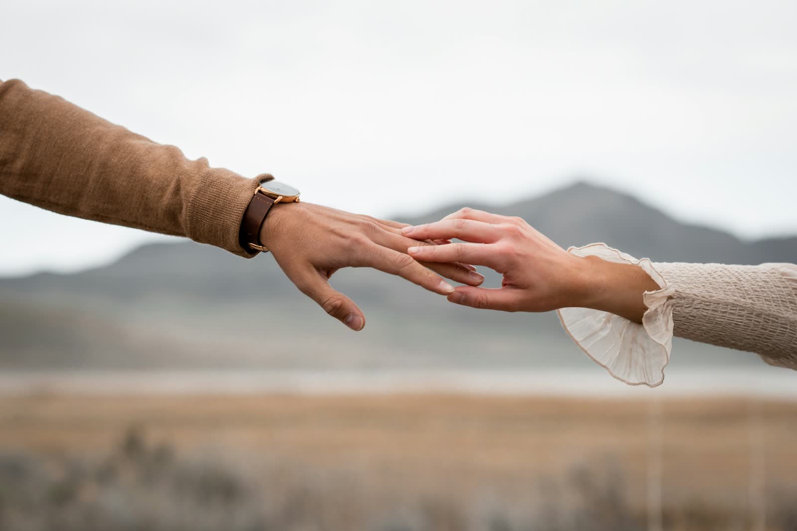 Two hands reaching toward each other, fingertips touching, close-up shot conveying quiet connection.